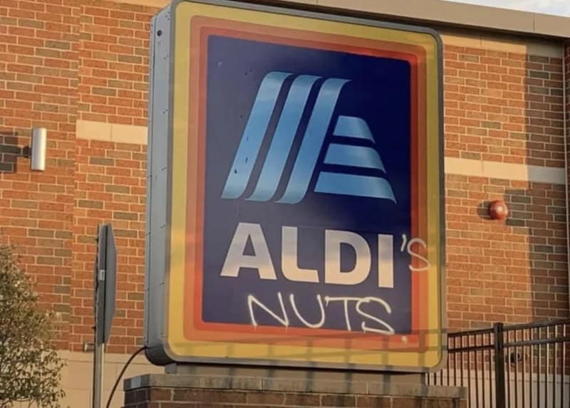 A sign for ALDI with graffiti reading 'NUTS' underneath.