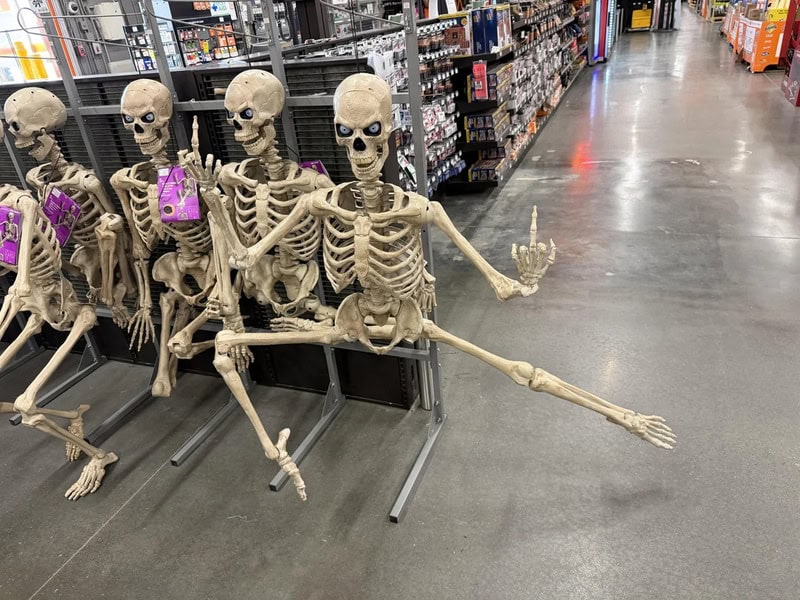 Group of skeleton decorations in a store aisle, some holding purple gift bags.