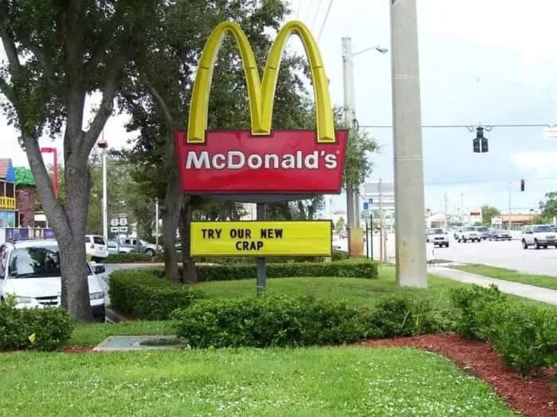 McDonald's sign with a yellow arch and a yellow sign below that says 'TRY OUR NEW CRAP'.