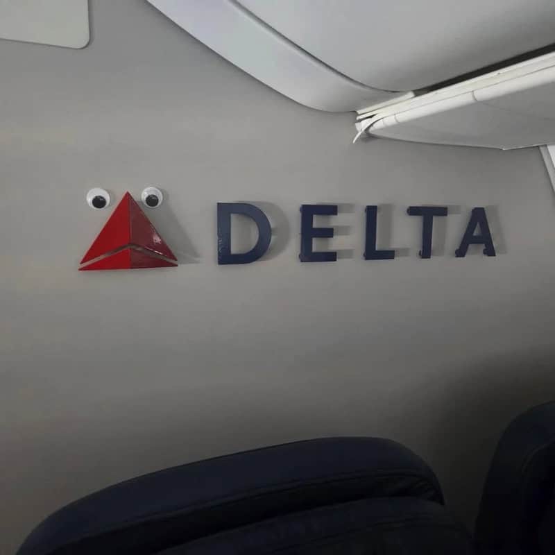 Googly eyes and a red triangle form a face next to the Delta logo on the wall.