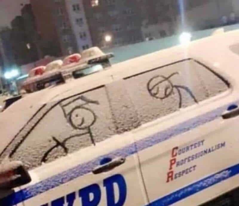 Police car with snow-covered windows and two stick-figure drawings on the snow.