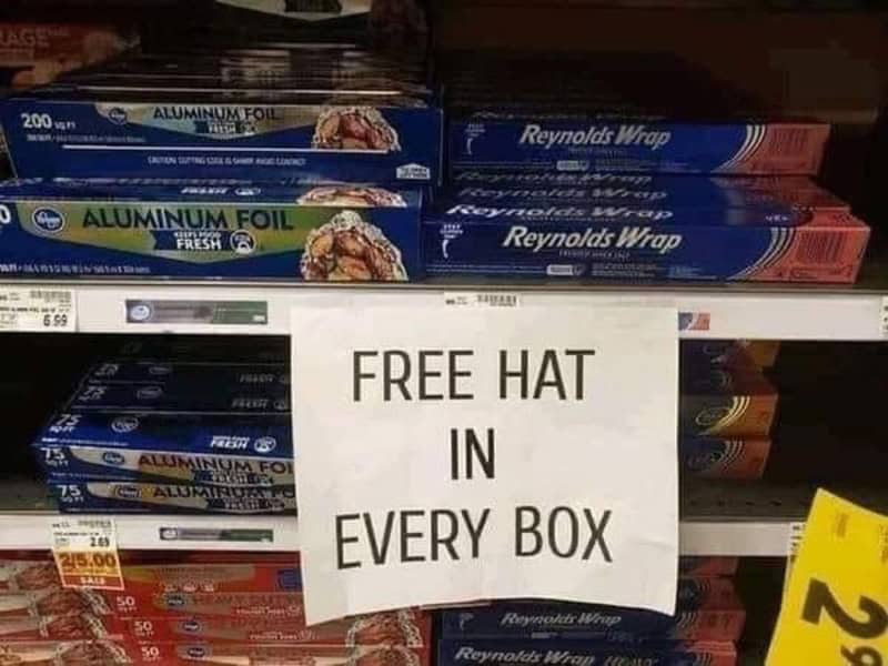 Sign reading 'FREE HAT IN EVERY BOX' on store shelf with aluminum foil boxes.