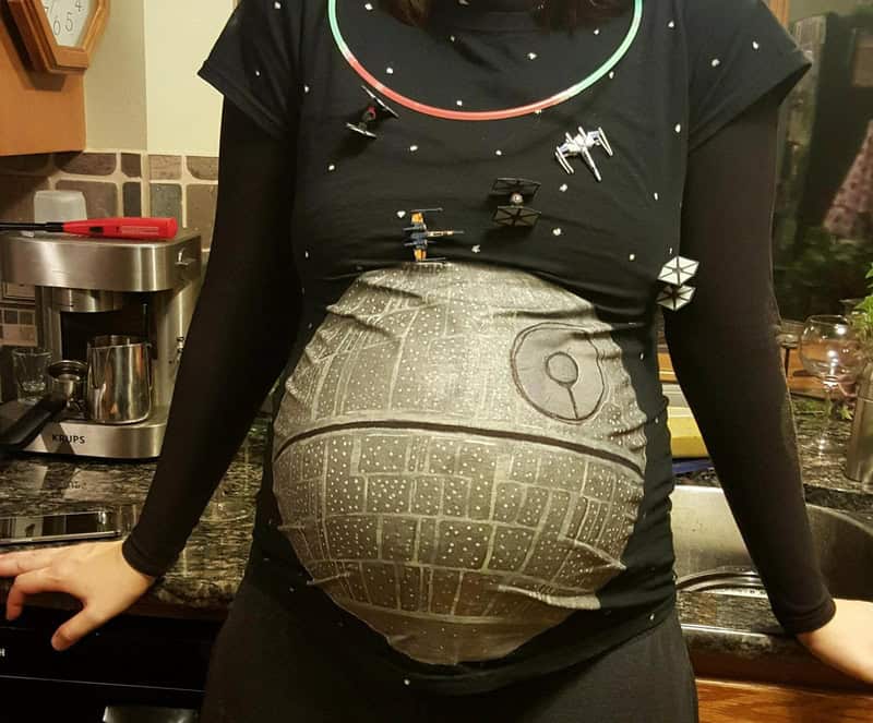 Pregnant woman in Star Wars costume with spaceship design on belly.