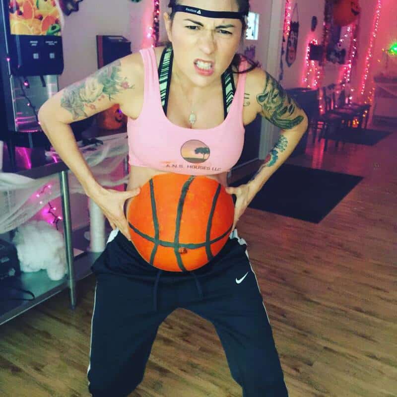 Pregnant woman with a basketball belly, making a fierce face in a decorated room.