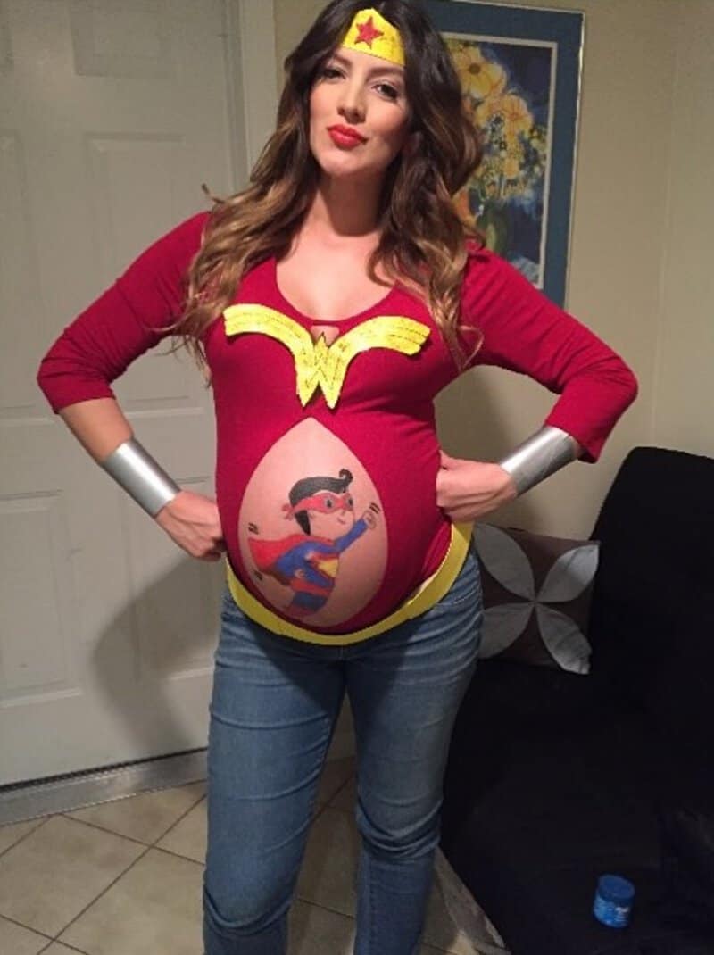 Pregnant woman in Wonder Woman costume with painted belly and costume accessories.