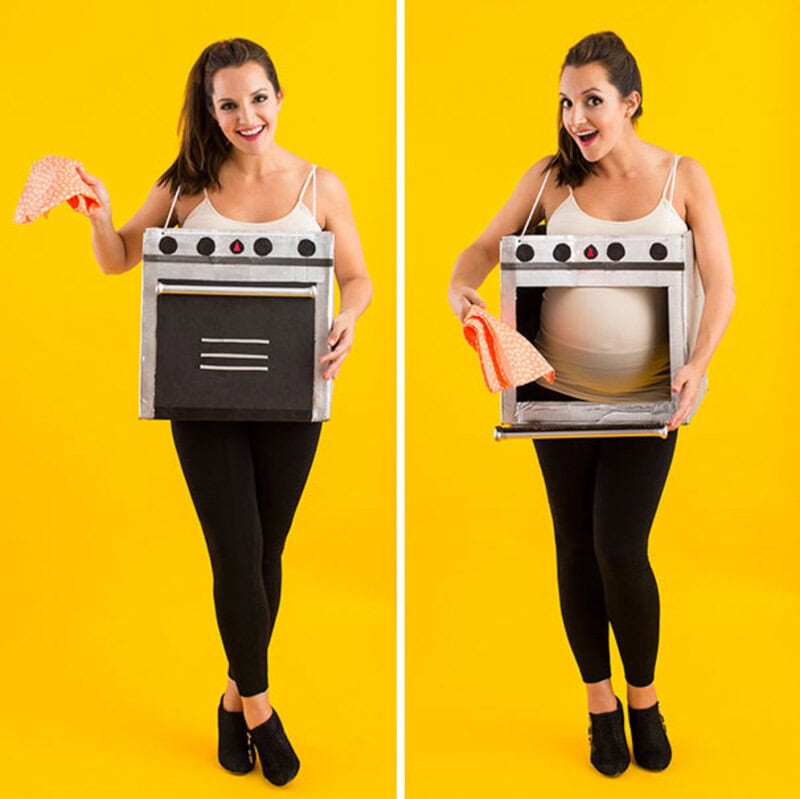 Pregnant woman in oven costume with oven door open, holding oven mitts, yellow background.