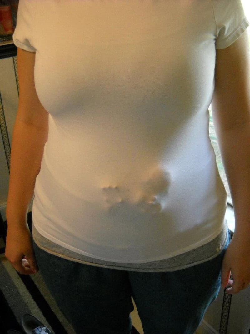 Pregnant woman in a white T-shirt with a baby bump, standing indoors.