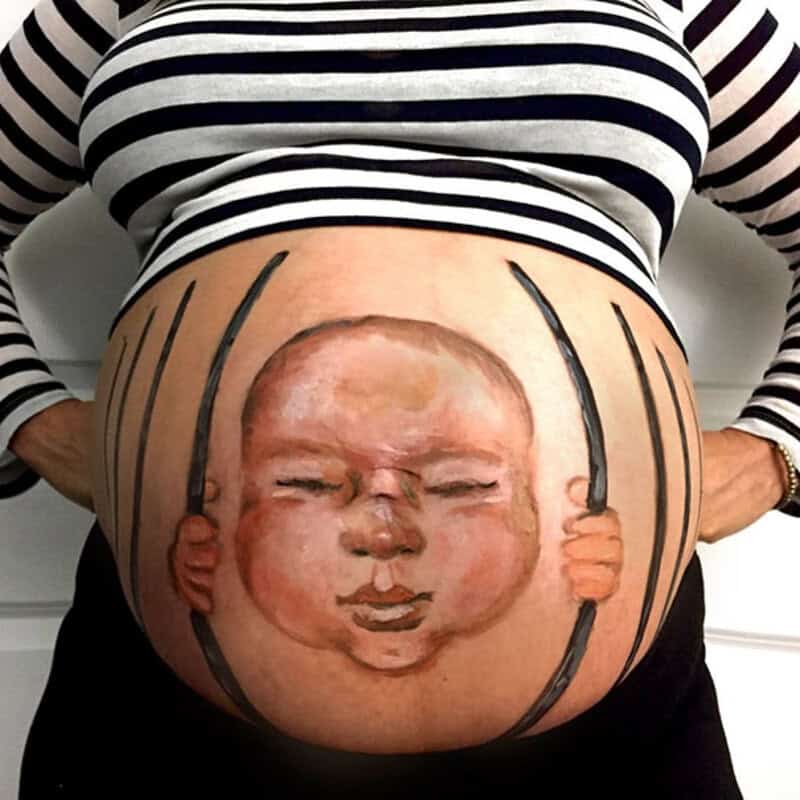 Pregnant belly with a face painted to look like a baby in a cradle.