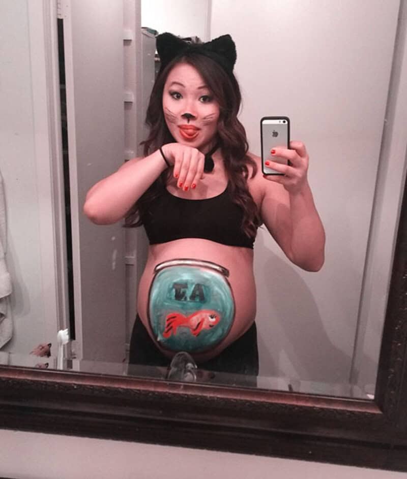 Pregnant woman with cat ears taking mirror selfie, sticking out tongue.