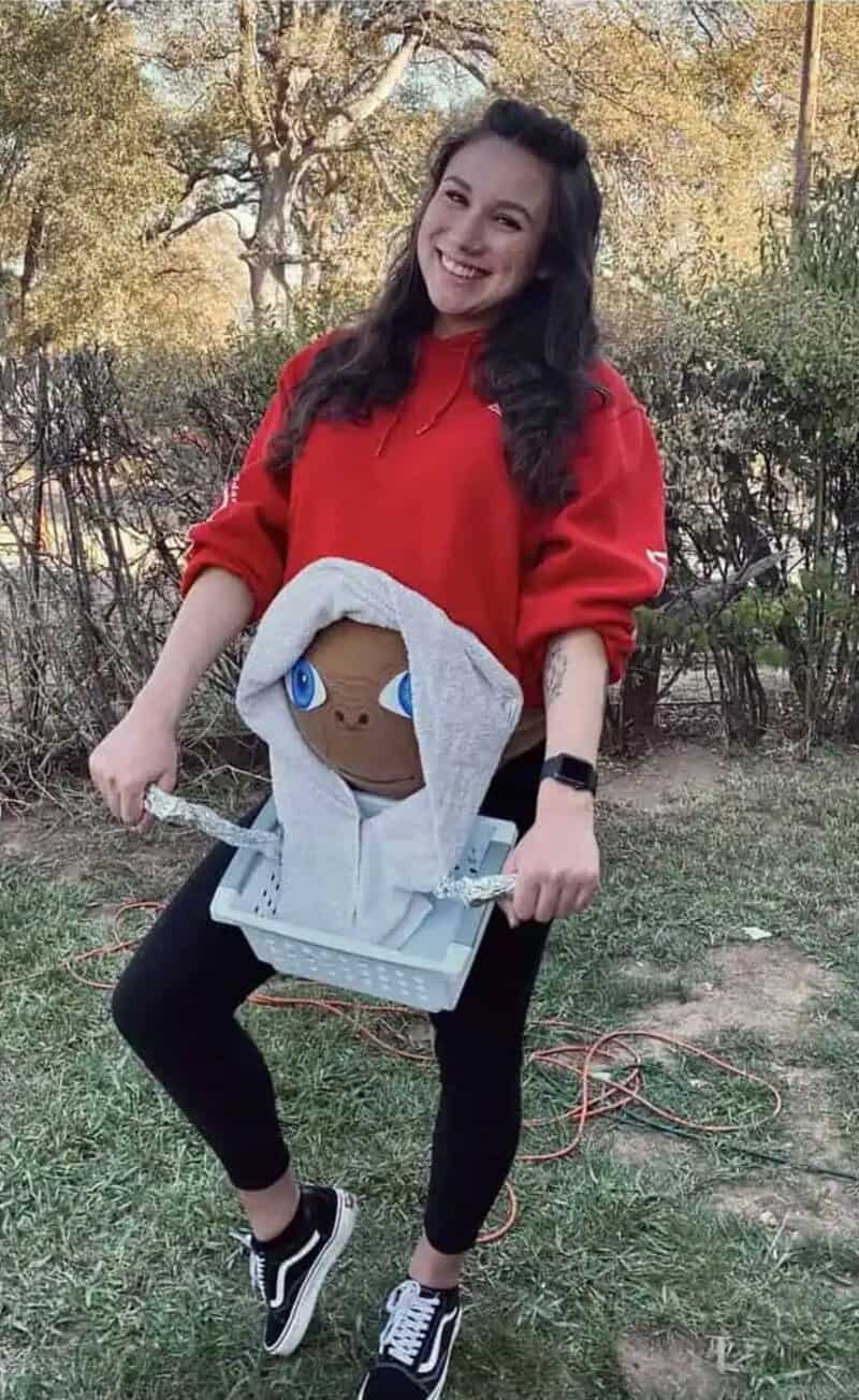 Woman in red sweatshirt holding a baby bump costume with a hoodie and cartoon face.