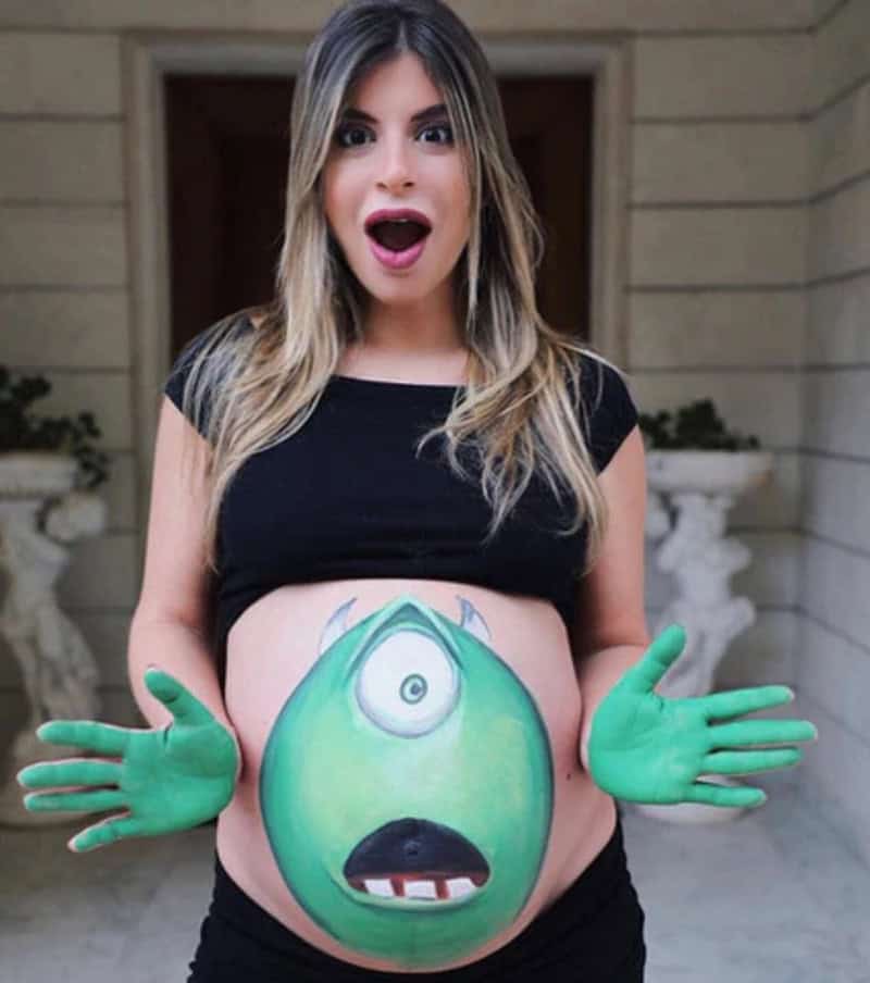 Pregnant woman with a painted green monster on her belly, surprised expression.