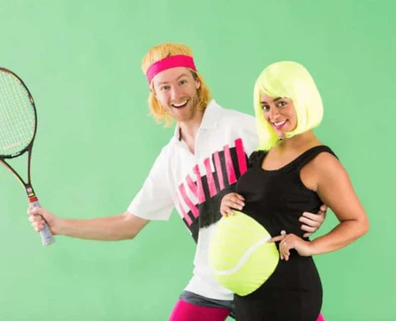 Couple in colorful 80s costumes with tennis racket and giant tennis ball.