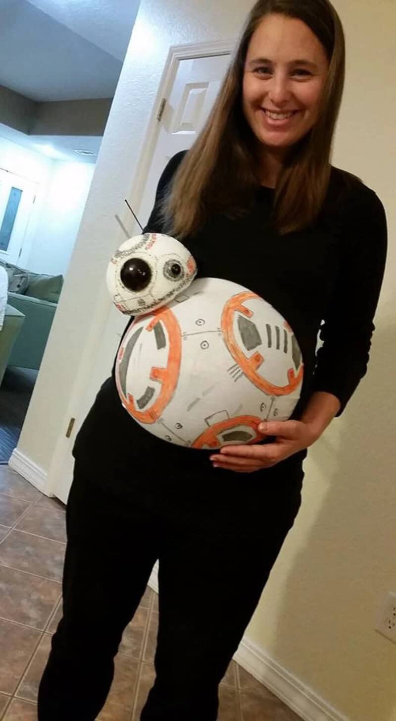 Pregnant woman holding BB-8 droid costume for Halloween.