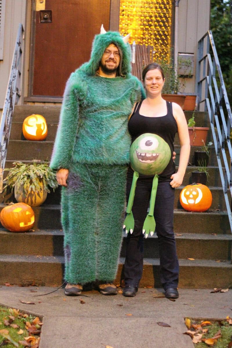 Person in a green furry monster costume with a woman holding a green monster-themed pumpkin.