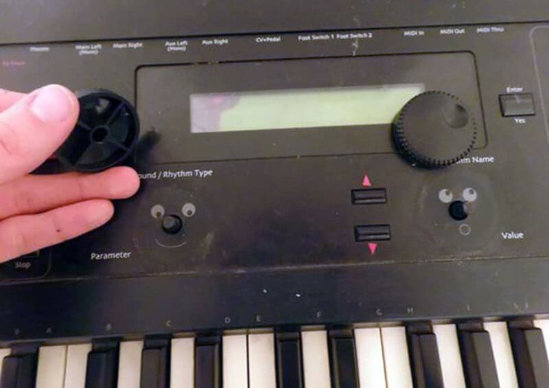 Close-up of a music keyboard with a hand adjusting a knob, part of a device with buttons and a small.