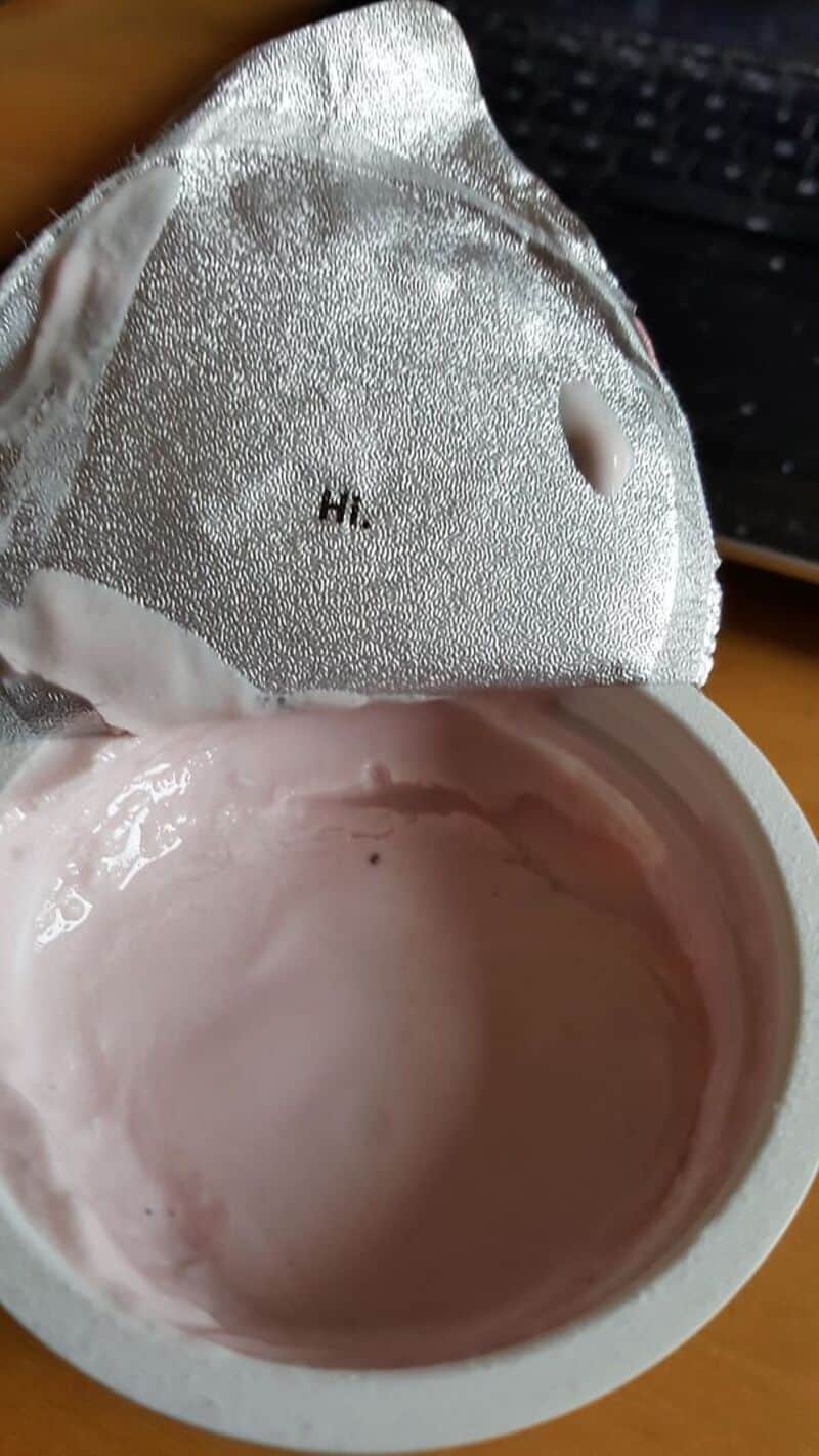 Open container of pink yogurt with foil lid partially peeled back.