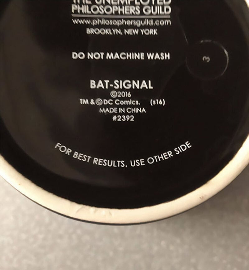 Close-up of a black and white coffee cup with text about Batman and washing instructions.