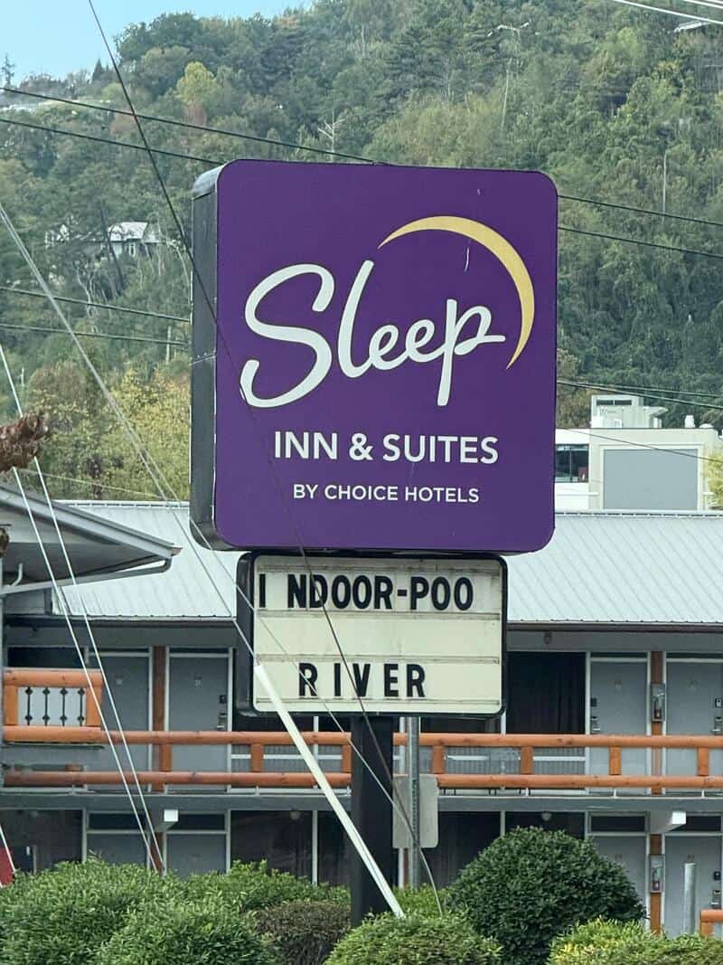 Sleep Inn & Suites sign with purple logo, outdoor signboard reading INDOOR-POO? RIVER in a hotel lot.