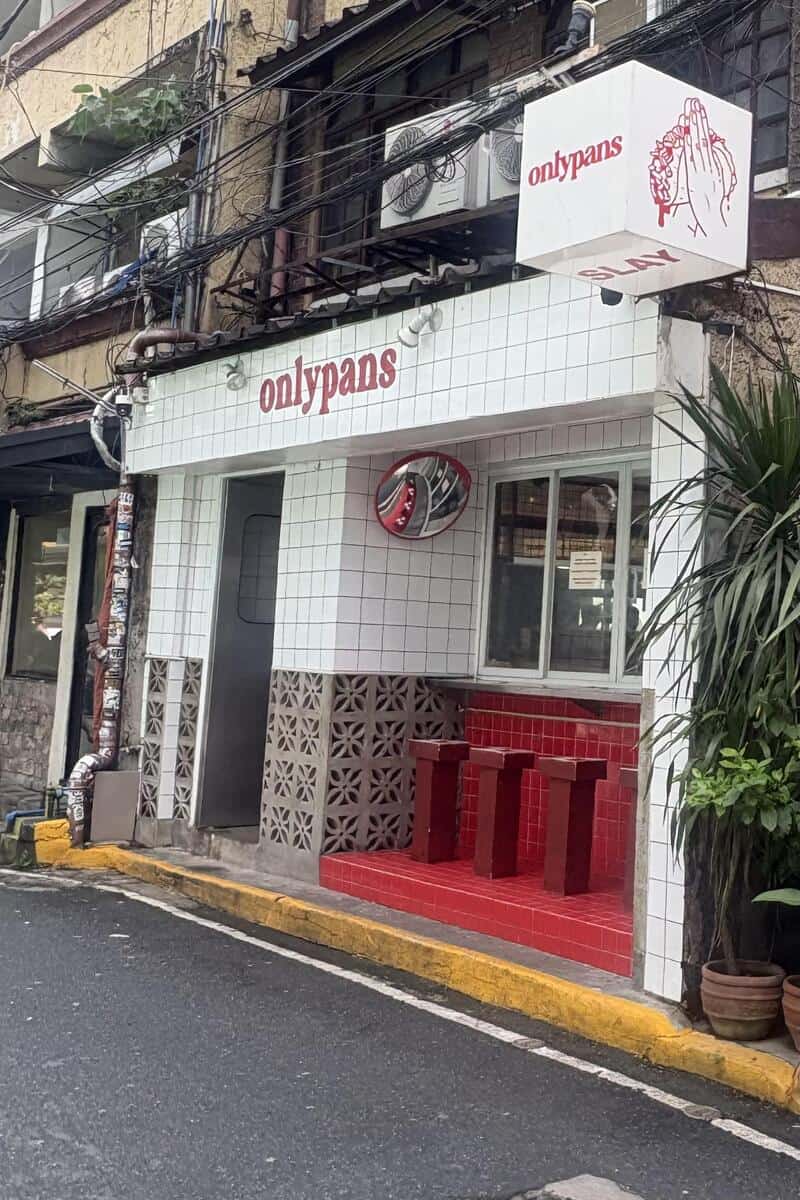 Onlypants store on a narrow street with white tiled facade and red seating area outside.
