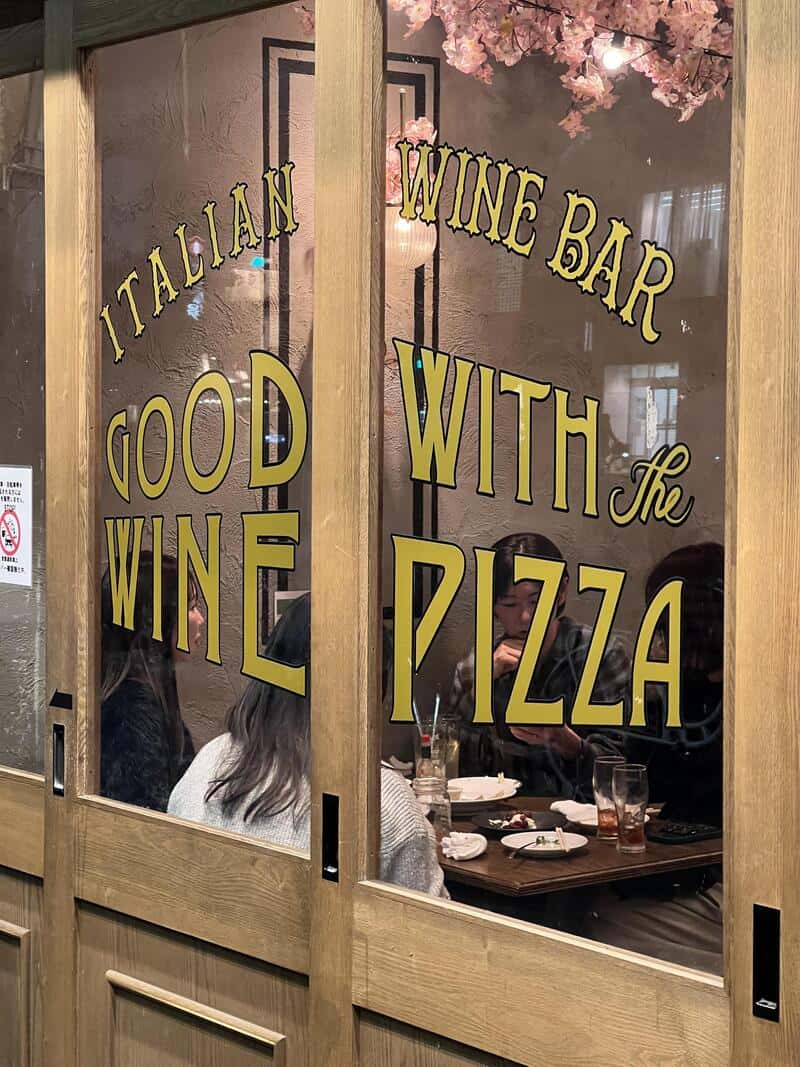 Italian wine bar good wine with pizza signage on glass door.