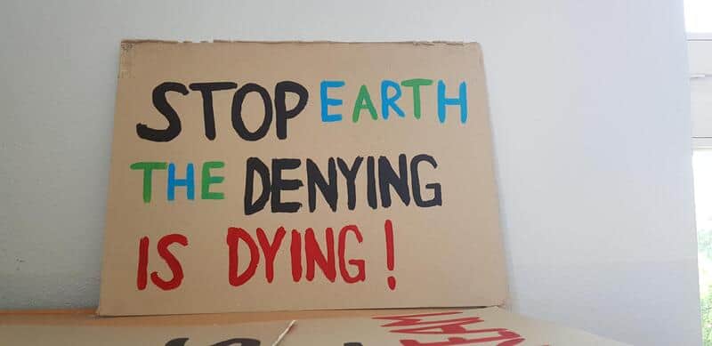 Stop Earth The Denying Is Dying! sign protesting environmental denial.