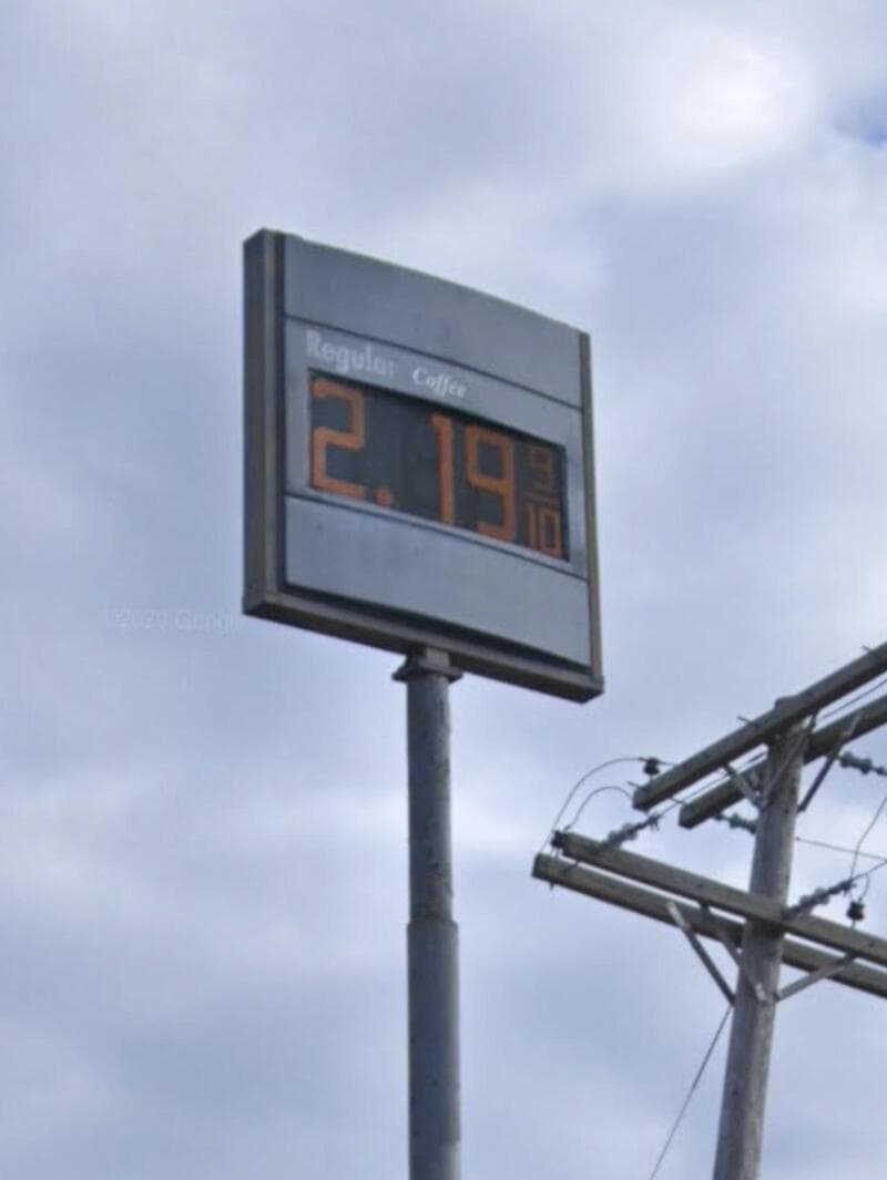 Fuel price sign showing 2.19 (currency not specified) with a cloudy sky and utility lines nearby.