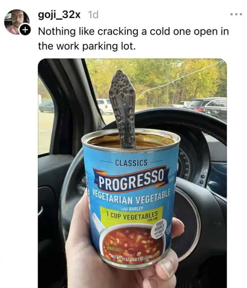 A hand holding a can of Progresso vegetarian vegetable soup in a car parking lot.