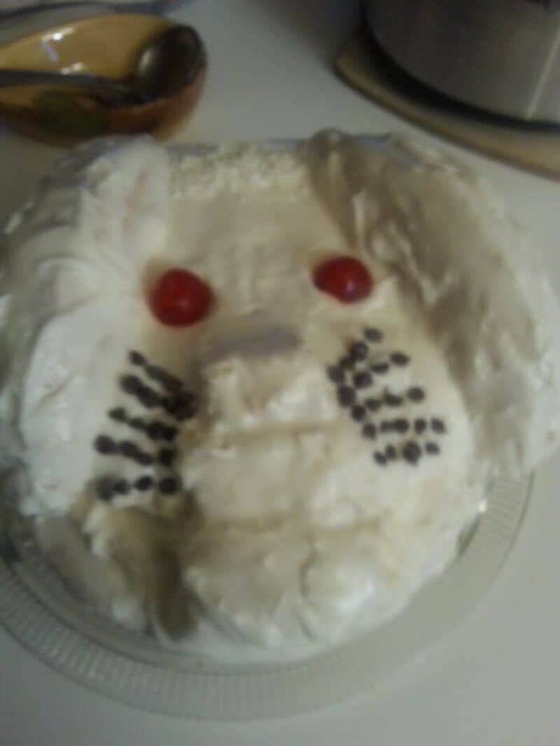 Hilarious cake decorated to resemble a white bunny face with red candy eyes and whisker dots on a pl.