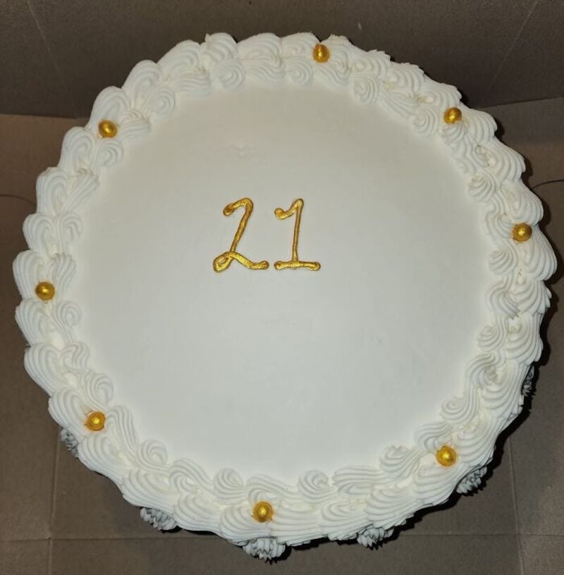 Hilarious cake with white frosting, gold number 21, decorative border and gold beads.