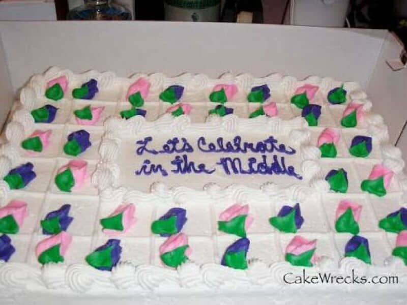 A large rectangular cake with white frosting and colorful pink, purple, and green floral decorations.