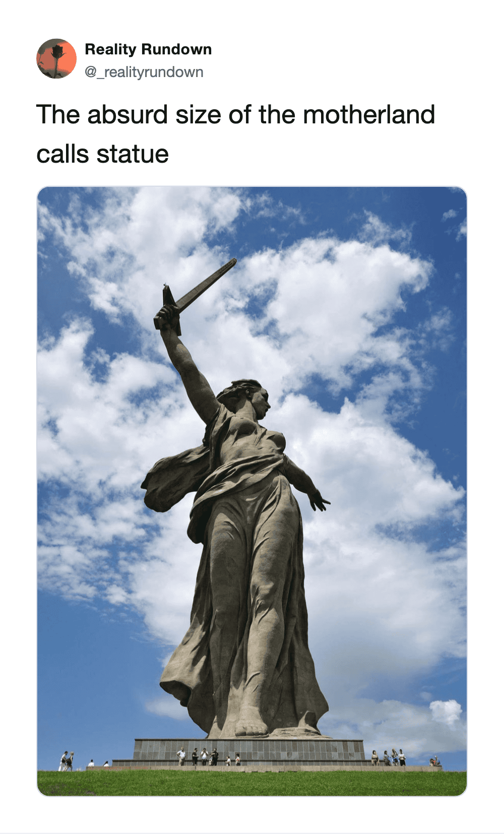 The Motherland Calls statue with a sword raised high against a blue sky with clouds.