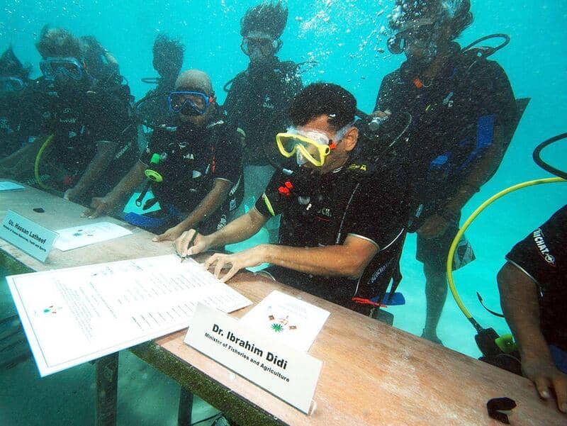 Group of scuba divers underwater with a person signing documents at a table.