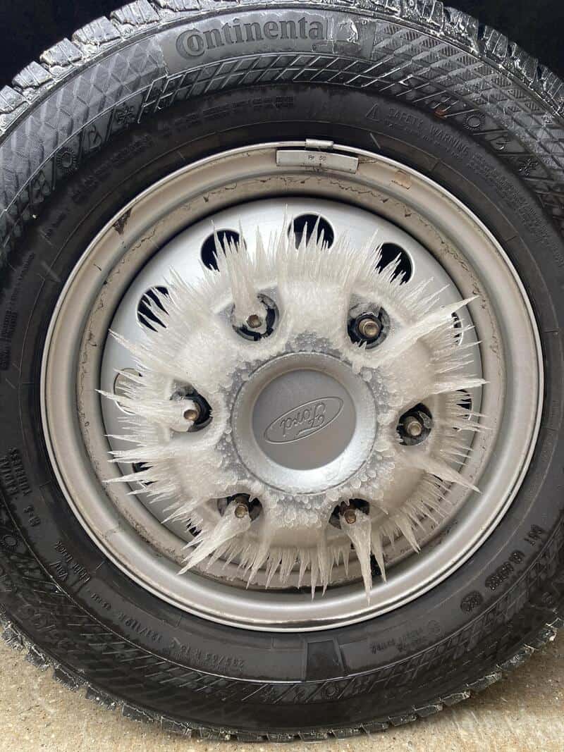 Car tire with ice and frost on the wheel cover and rim.