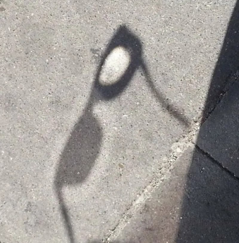 Shadow of a street lamp on a concrete sidewalk with a shadow of a building edge.