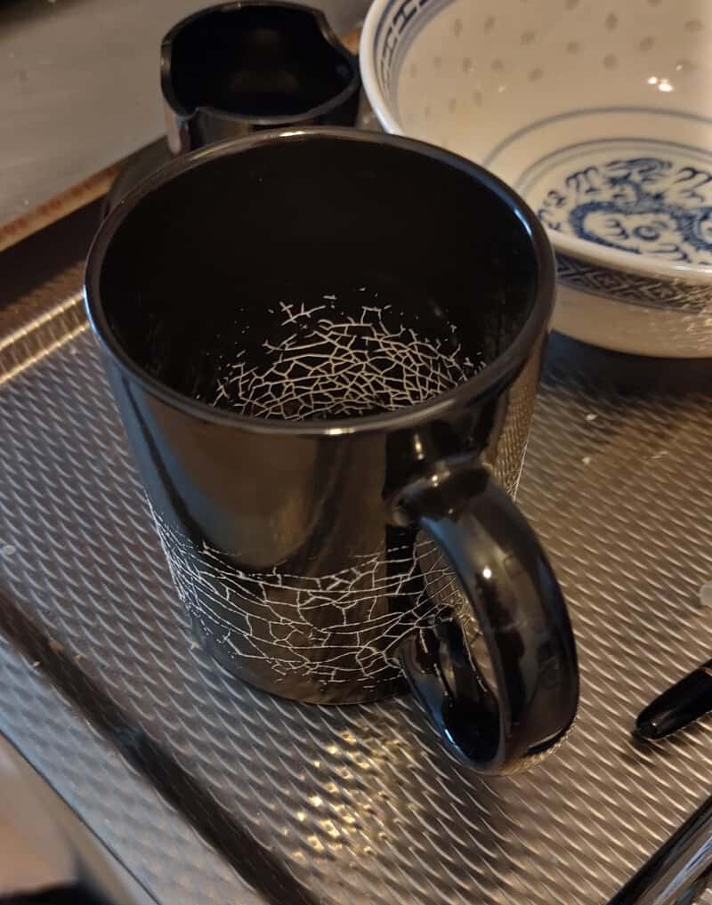 Black mug with a crackled white pattern, empty inside, on a metal surface.