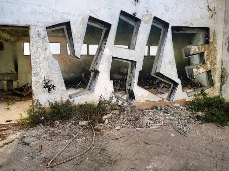 Abandoned building with large broken mirror letters spelling 'THE' on the wall.