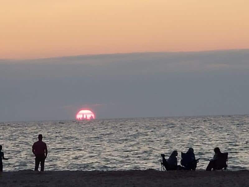 Sunset over the ocean with silhouettes of people on the beach.