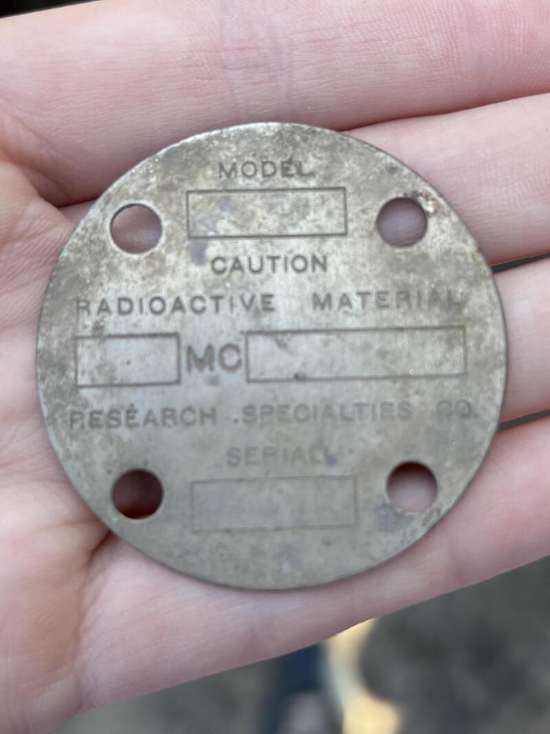 Round metal tag with text and four holes, held in hand.