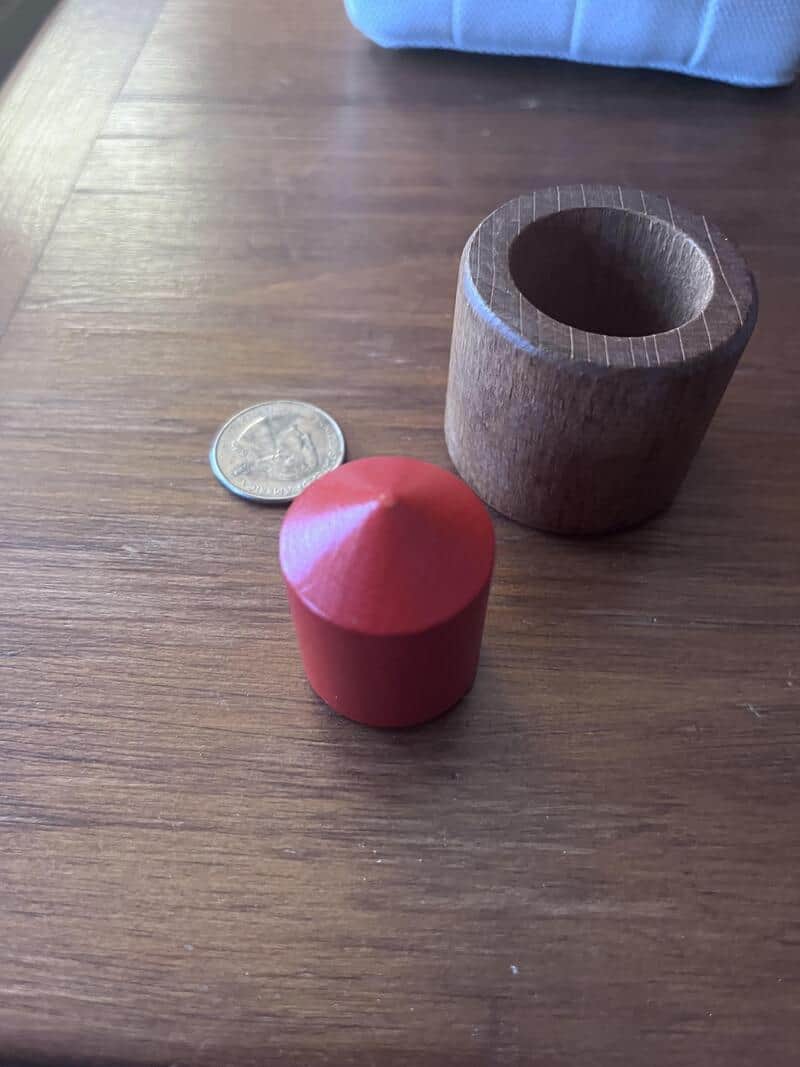 Wooden cylinder with hollow center, red cone, and quarter on wooden table.
