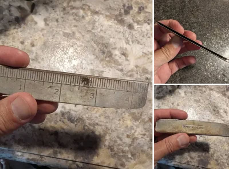 Hand holding a small, thin, black object, possibly a needle or pin.