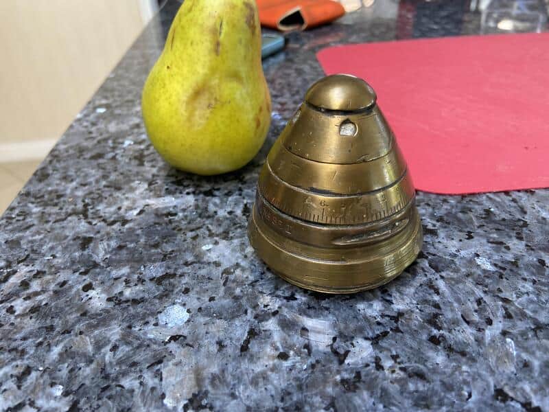 Pear and a brass pepper grinder on a kitchen countertop.