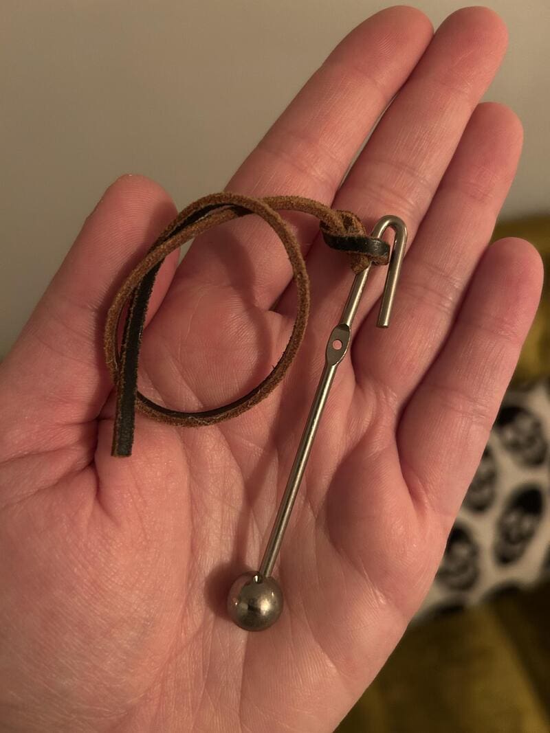 A metal pin with a leather strap attached, held in a person's hand.