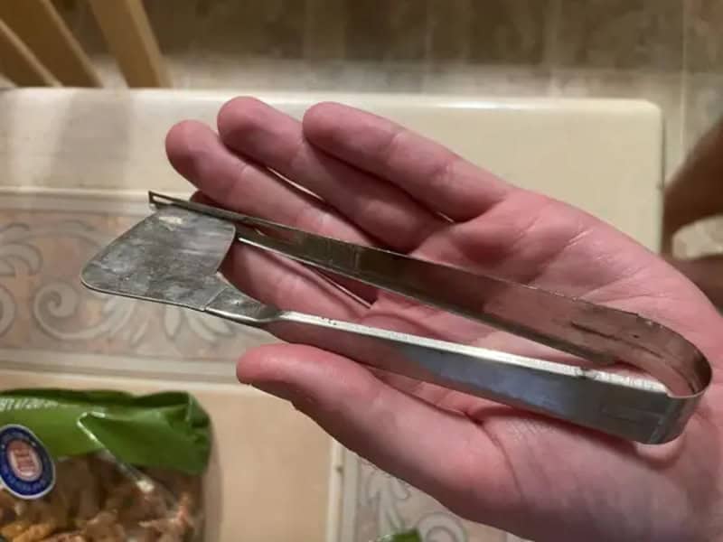 A hand holding a metal tool with a flat, curved end in a kitchen setting.