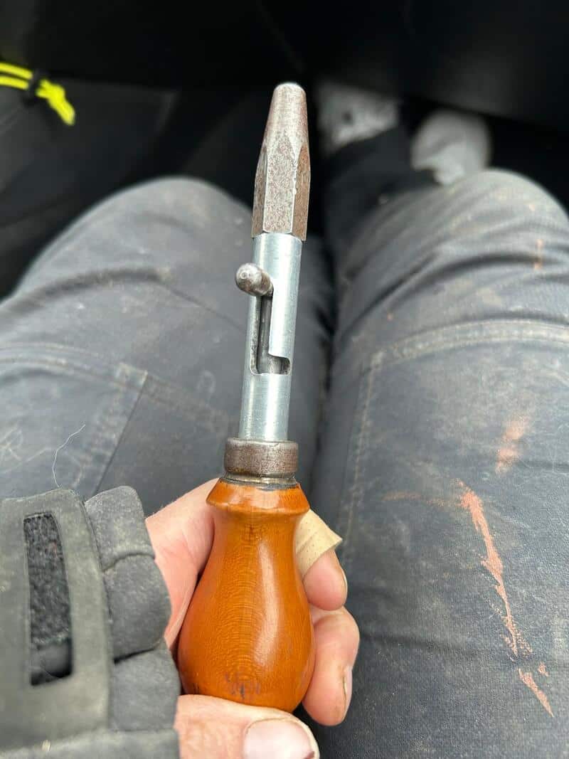 A hand holding a chisel with a wooden handle and metal blade.