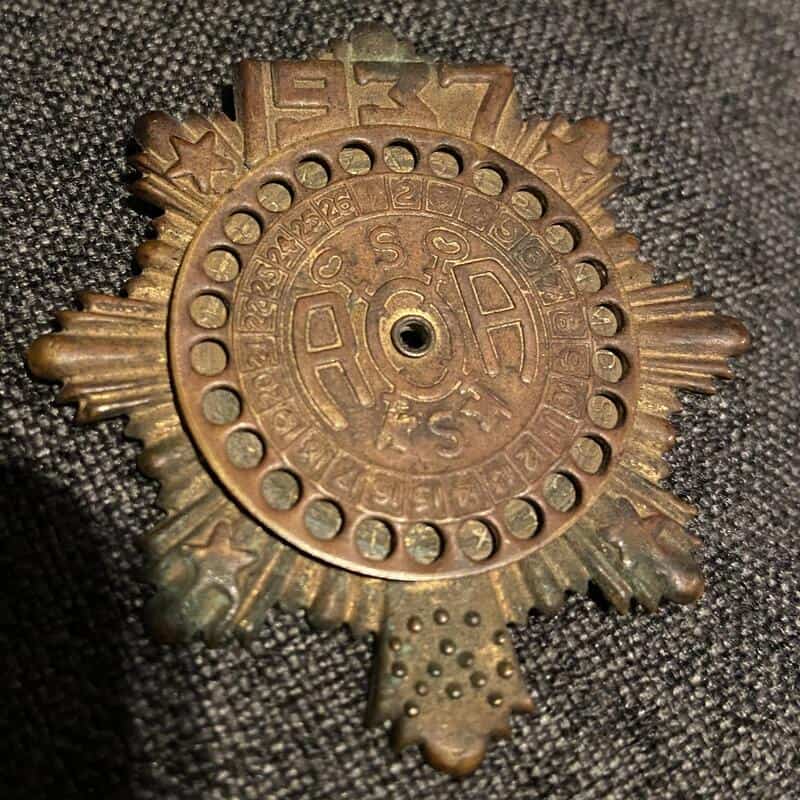 Close-up of a metallic badge with intricate symbols and a central hole.