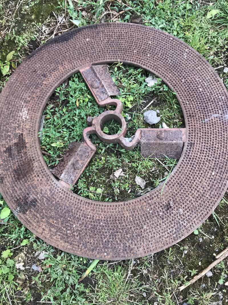 Rusty metal manhole cover with a central lock, on grass and dirt.