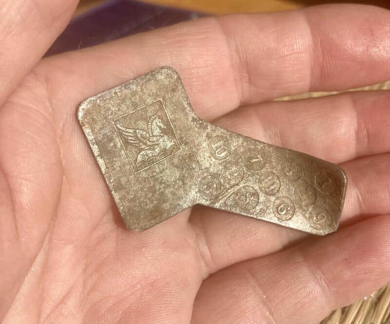 A worn, metallic object with a winged emblem and circular markings, held in a person's hand.