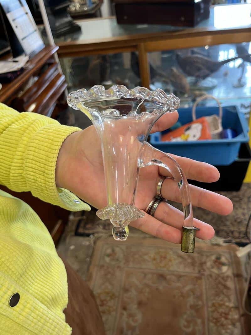 Glass vase with a handle, held by a person in a yellow sweater.