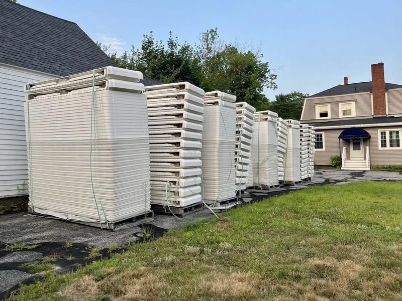 Multiple stacked white portable air conditioning units outside a house.