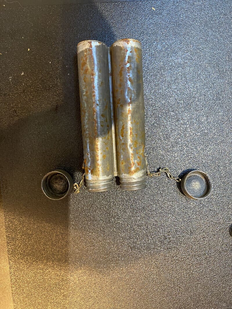 Two rusty cylindrical metal objects with attached small black caps on a black surface.